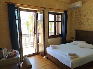 A hotel room with a bed, a desk with a chair, a window with curtains, and an air conditioning unit. - The Sea Front Rooms and Apartments (Rethymno)