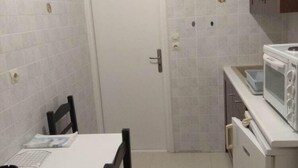Una cocina compacta con armarios blancos, un microondas y un comedor con una mesa y sillas.