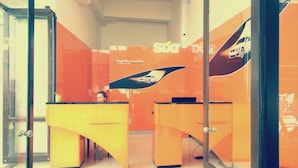 Ett kontorsutrymme med orange väggar, en glasdörr och en person som sitter vid ett gult skrivbord.