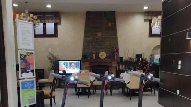 Tre elsparkcyklar står parkerade i en lobby med en öppen spis, en tv och en receptionsdisk.