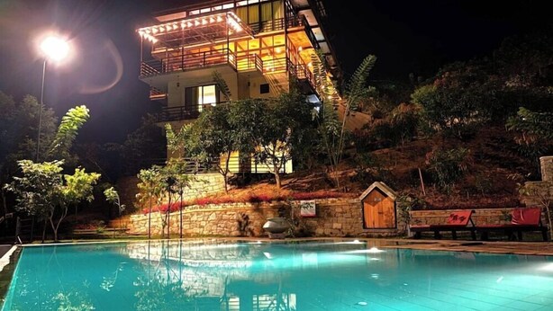 A modern building with a swimming pool at night, surrounded by trees and a stone wall. - Aqua Dunhinda Villa & Nature Retreat (Gampola)