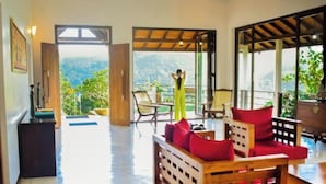 A spacious room with a wooden sofa, a dining table, and chairs. There is a large window providing a view of the outdoors. - Aqua Dunhinda Villa & Nature Retreat (Gampola)