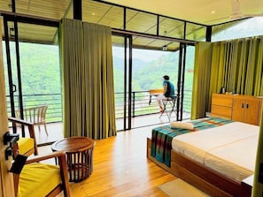 Quarto com cama, escrivaninha e cadeira, varanda com vista para as montanhas e piso de madeira.