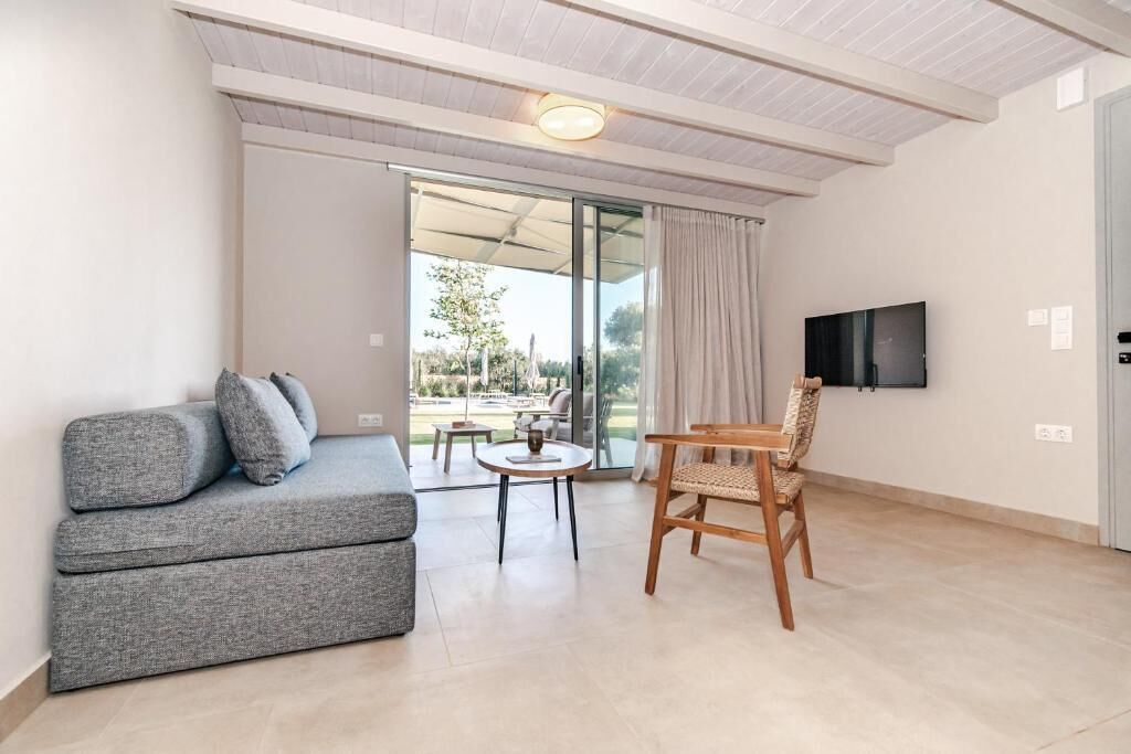 A modern living room with a grey sofa, a wooden chair, a small table, and a TV mounted on the wall.
