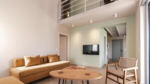 Un salon moderne avec un canapé, une table basse ronde en bois et un fauteuil en osier. Un téléviseur à écran plat est fixé au mur.