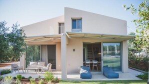 Une maison moderne à deux étages, dotée d’un patio couvert, d’un espace salon extérieur et d’un jardin bien entretenu.