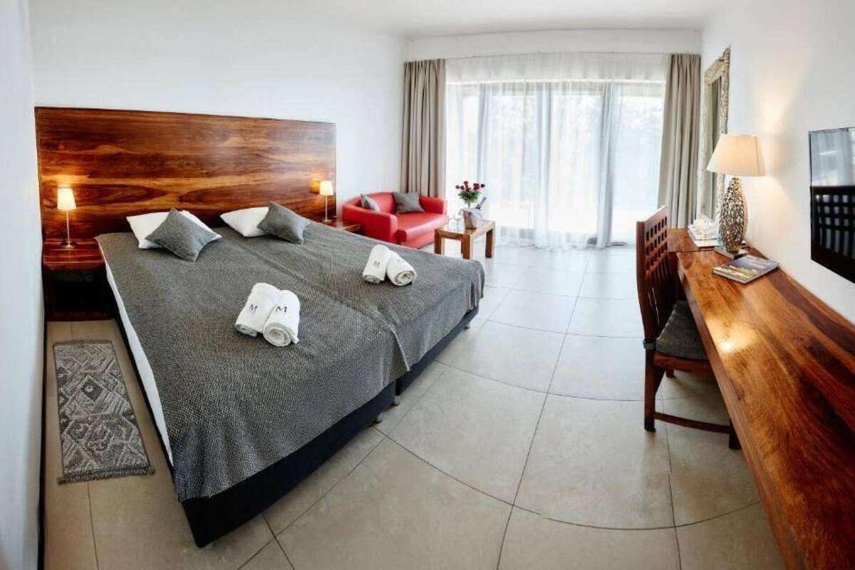 A hotel room with a large bed, a desk, a TV, and a red sofa.