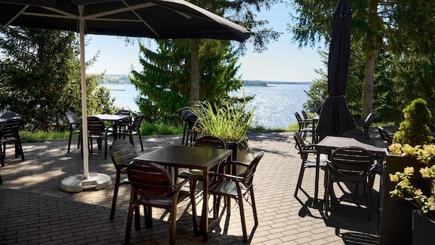 An outdoor patio with tables and chairs, a grill, and a view of a lake. - M Club Hotel  (Drawsko Pomorskie)