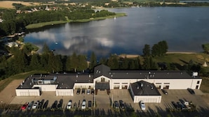 An aerial view of a building with multiple parking spaces and a large body of water in the background. - M Club Hotel  (Drawsko Pomorskie)
