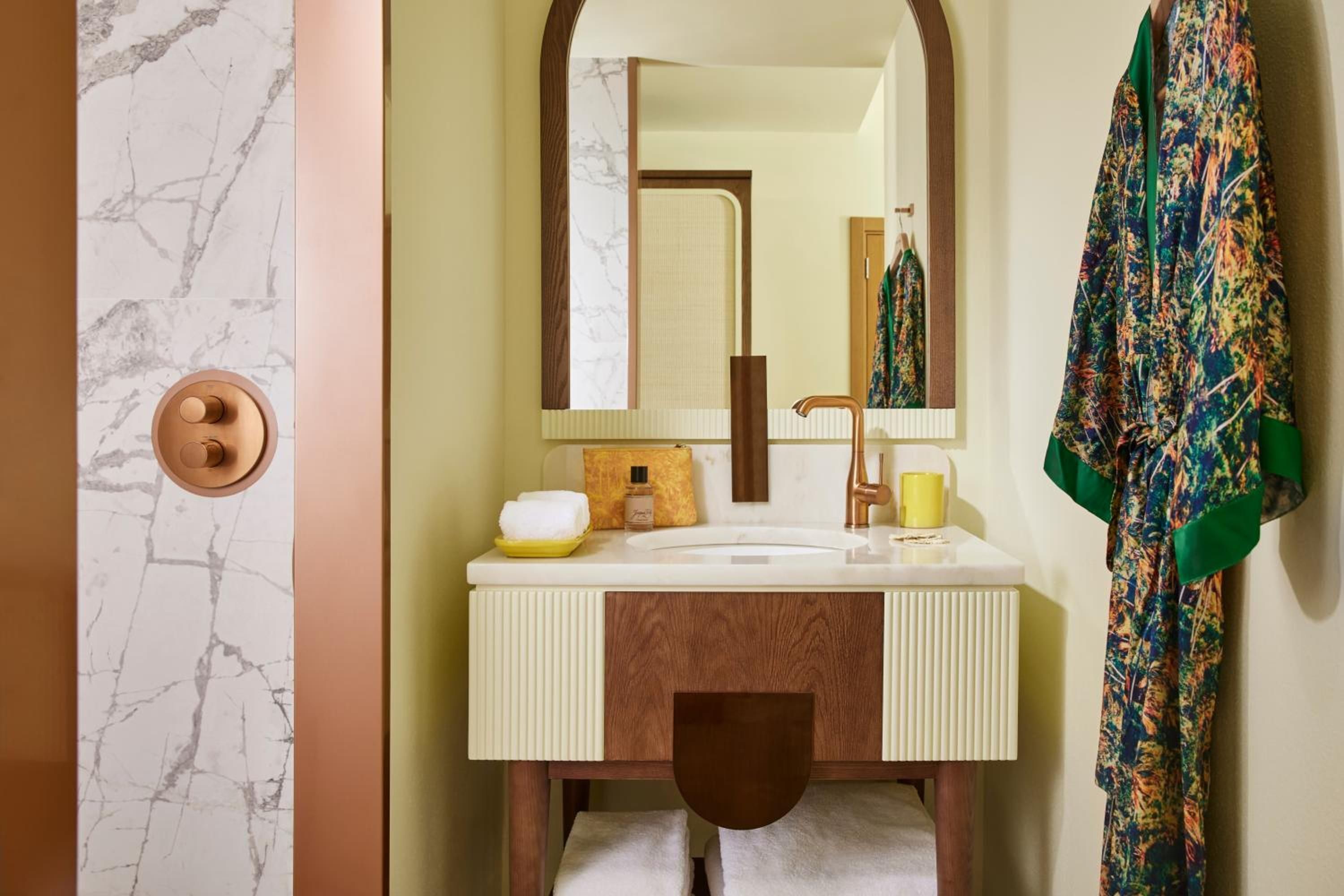 A bathroom with a marble wall, a sink, a mirror, a towel, and a robe hanging on the wall.