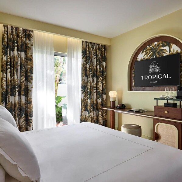 A hotel room with a bed, a desk with a lamp, a mirror, and curtains with a tropical print. - Tropical Hotel And Beach (St. Barthelemy)