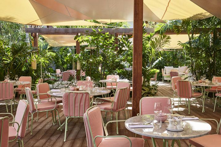 An outdoor dining area with round tables and chairs, surrounded by lush greenery.