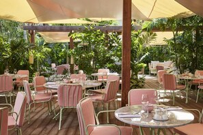 An outdoor dining area with round tables and chairs, surrounded by lush greenery.