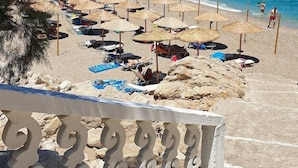 A beach with sun loungers and umbrellas, a staircase leading down to the beach, and boats in the water. - Althea Boutique Hotel (Karpathos)