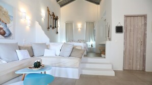 A spacious living area with a sofa, a small round table, and a staircase leading to a bedroom. - Althea Boutique Hotel (Karpathos)