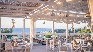 An outdoor dining area with white furniture and a view of the sea. - Althea Boutique Hotel (Karpathos)