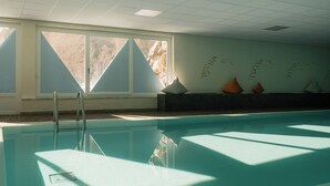 Una piscina interior con paredes de vidrio transparente, una escalera y vistas a un paisaje montañoso a través de amplios ventanales.