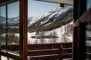 Une vue depuis une fenêtre à cadre en bois, donnant sur un paysage montagneux enneigé avec une station de ski et des bâtiments.