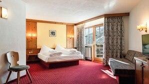 Una habitación de hotel con cama, una silla, un sofá, televisión y ventana con cortinas.