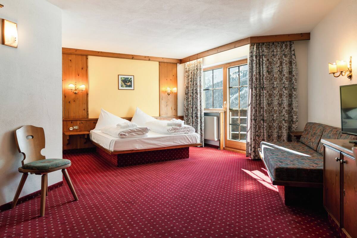 A hotel room with a bed, a chair, a sofa, a TV, and a window with curtains.