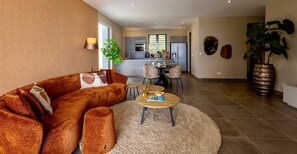 A modern living room with a sofa, coffee table, and a dining area with chairs and a table. - Luxury ground-floor apartment with tropical calm (Sint Willibrordus)