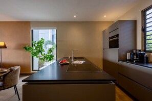 A modern kitchen with a central island, built-in appliances, and a view of greenery outside. - Luxury ground-floor apartment with tropical calm (Sint Willibrordus)