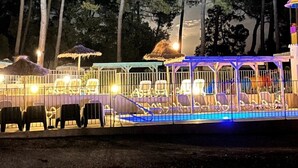 Un espace extérieur aménagé pour la nuit, avec une piscine, des chaises longues et des parasols.