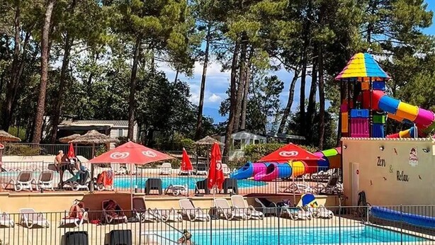 Un espace piscine équipé de chaises longues, de parasols et d’un toboggan aquatique.