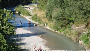 Une rive de rivière où l’on peut voir des gens pratiquer diverses activités, le tout étant entouré d’une végétation luxuriante.