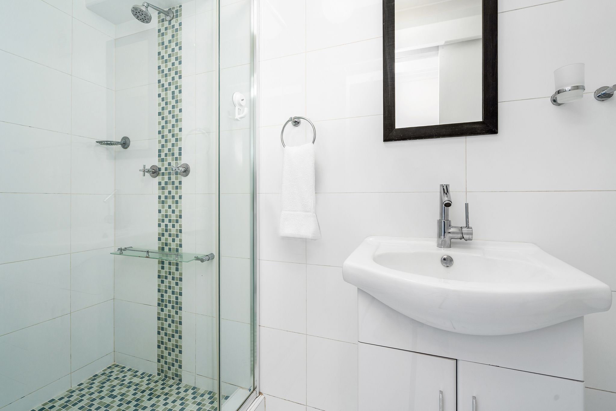 A modern bathroom with a glass shower enclosure, a white sink, and a mirror.