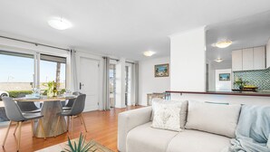 A modern living room with a sofa, dining table, and chairs. There is a kitchen area with cabinets and a countertop. - Coral Island G01 (Cape Town)