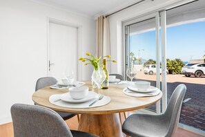 A dining area with a round table, chairs, a vase with flowers, and a view of the outside. - Coral Island G01 (Cape Town)