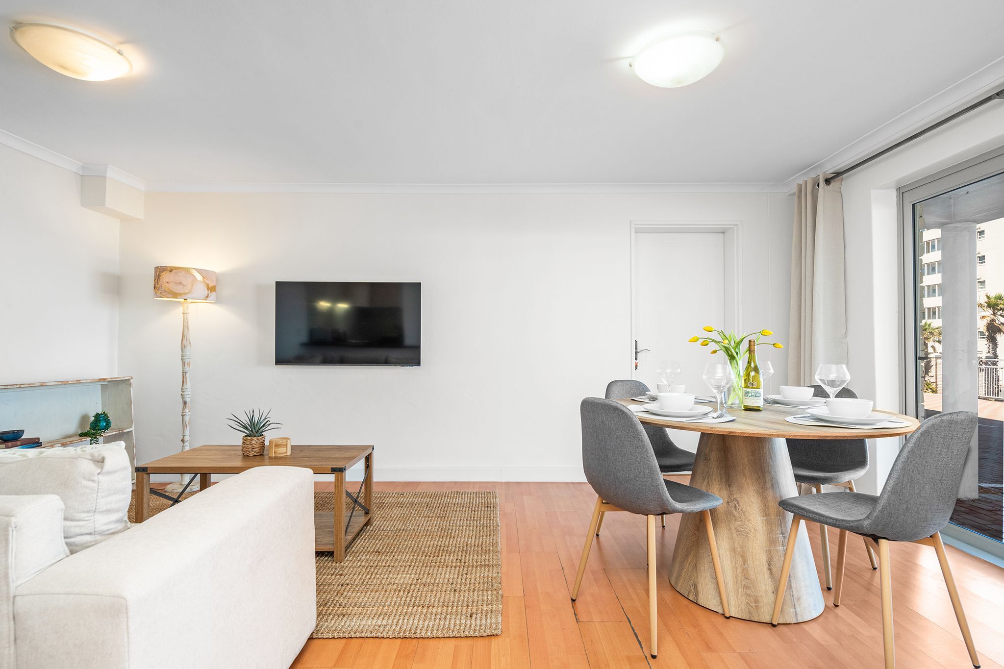 Ein modernes Wohnzimmer mit einer Couch, einem Esstisch mit Stühlen, einem flachbildfernseher an der Wand und einem großen Fenster mit Blick.