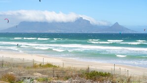 A beach with waves, a mountain, and kites in the sky. - Coral Island G01 (Cape Town)