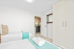 A hotel room with two beds, a kitchenette, and a wardrobe. - Coral Island G01 (Cape Town)