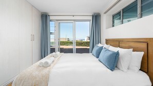 A hotel room with a large bed, a wooden headboard, a view through a glass door, and a balcony. - Coral Island G01 (Cape Town)