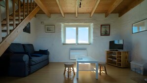 Ein gemütliches Wohnzimmer mit einer Holztreppe, einem Sofa, einem Tisch, einem Fernseher und einem Fenster.