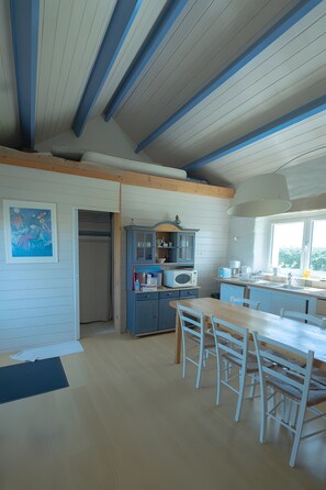 A kitchen with a wooden table and chairs, a cabinet, and a window. - The Island’s Former Gonio Station: Panoramic Sea Views and Cozy Comfort (Ouessant)
