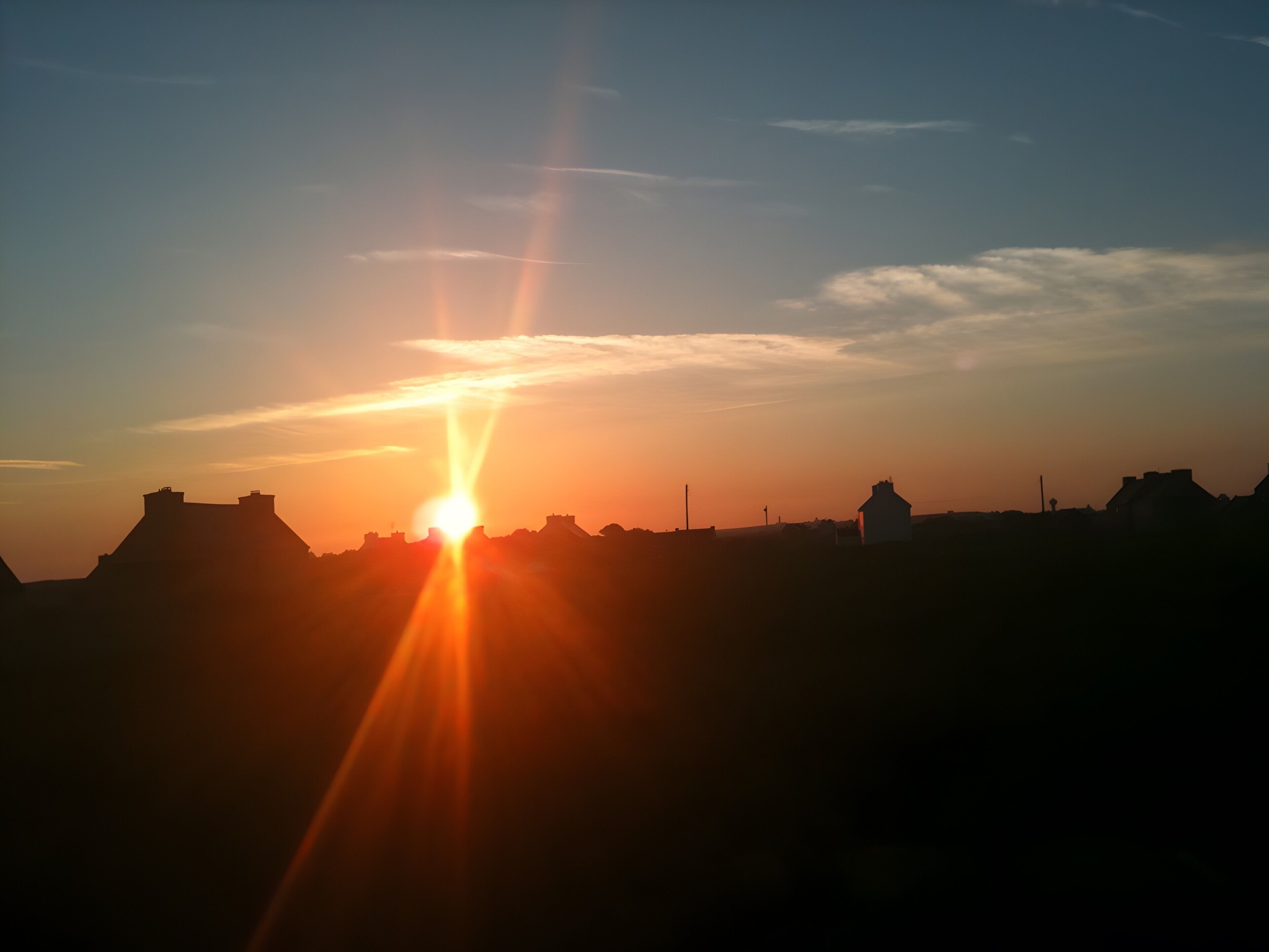 A sunset over a flat landscape with silhouettes of buildings and a prominent hill.