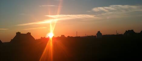 A sunset over a flat landscape with silhouettes of buildings and a prominent hill.