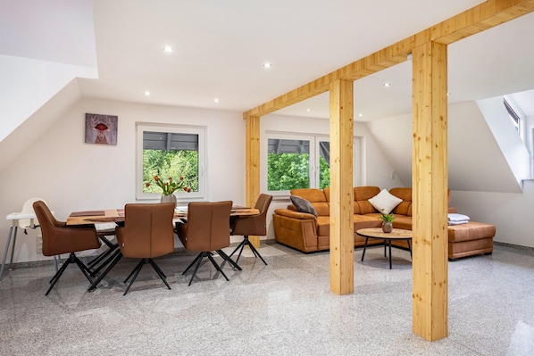 A modern interior with a dining area, sofa, and wooden beams.