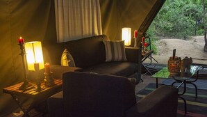 Ett mysigt tält med en soffa, två sidobord med ljus, ett glasbord med ett ljus och utsikt över omgivningen.