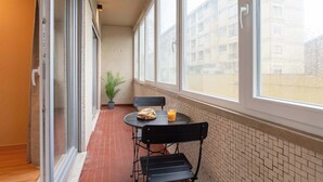 Een balkon met een tafel, stoelen, een bloempot en een raam met uitzicht op een gebouw.