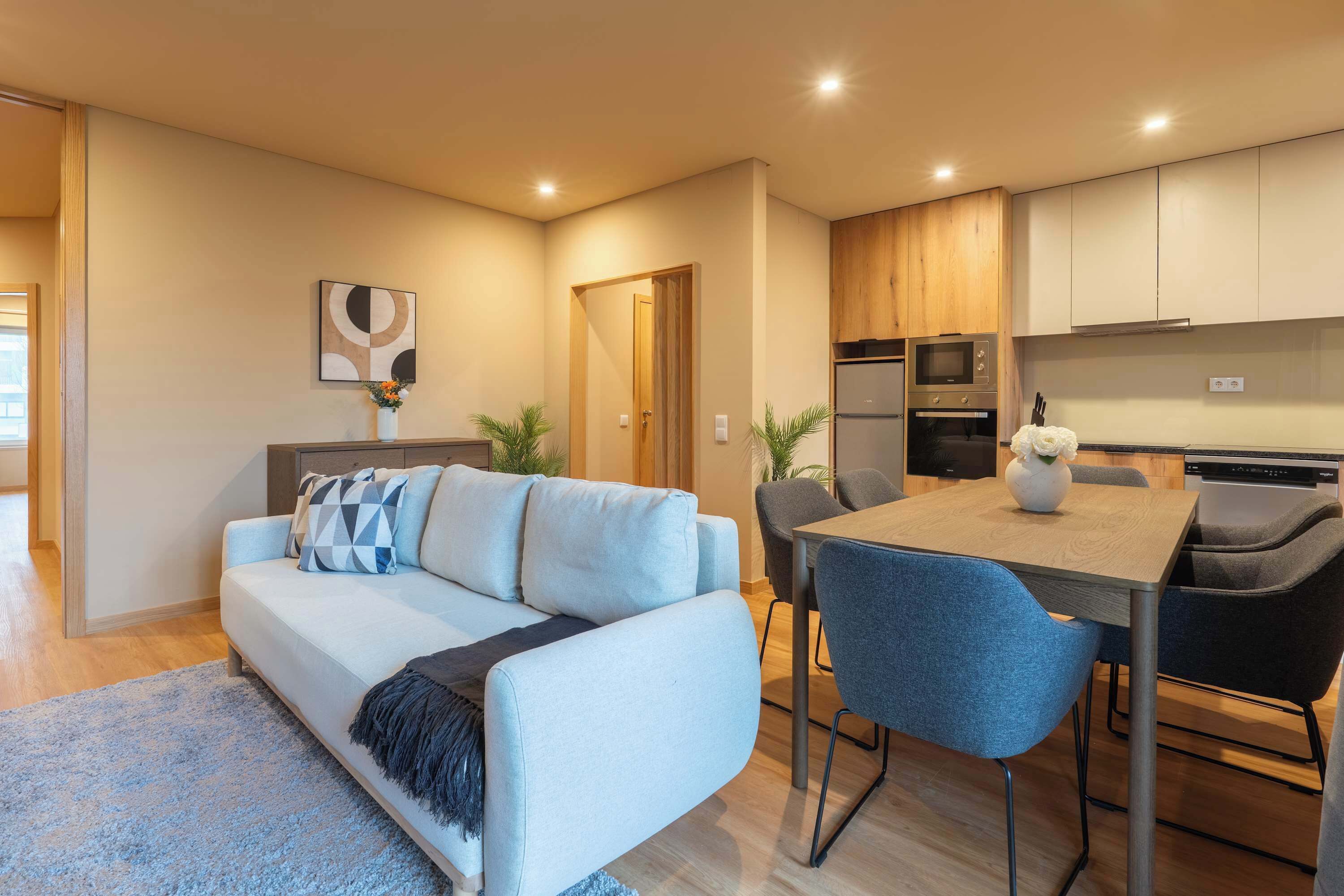 A modern living room with a light blue sofa, a coffee table, and a dining area with a wooden table and chairs.