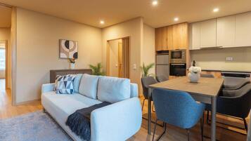 A modern living room with a light blue sofa, a coffee table, and a dining area with a wooden table and chairs.