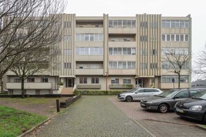 Un immeuble résidentiel à plusieurs étages, doté d’une allée pavée et de voitures garées.