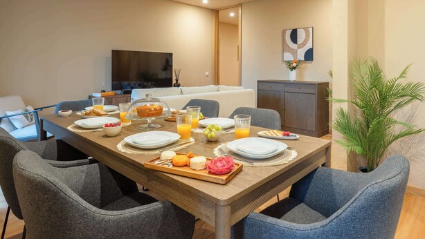 Een ontbijtruimte met een houten tafel, gedekt met borden, glazen en een schaal fruit.