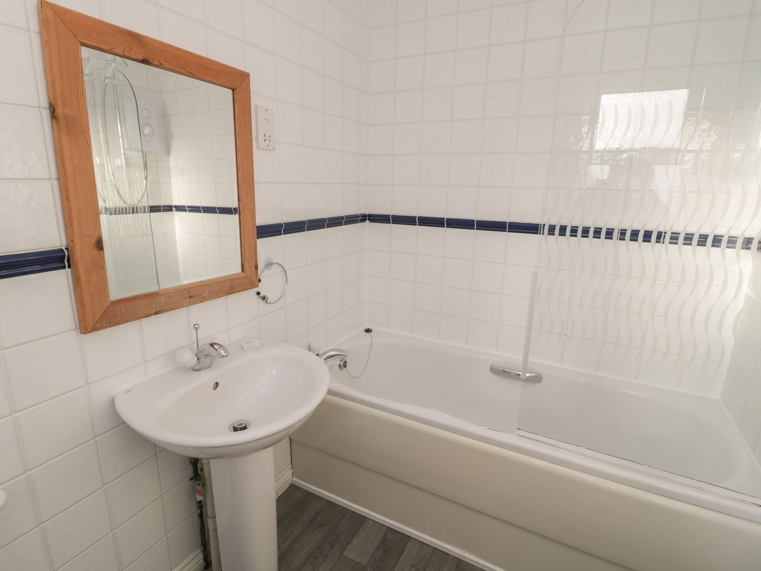 Un baño con un lavamanos blanco, un espejo con marco de madera y una bañera con detalles de azulejos azules.