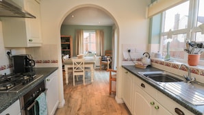 A kitchen with a stove, oven, and sink. There is a dining area with a table and chairs. - Sandy Cove (Chathill)