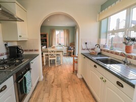 Una cocina con estufa, horno y lavaplatos. Hay una zona de comedor con una mesa y sillas.